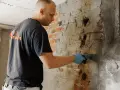 Mann verputzt feuchten Kellerwand.
