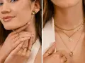 Uśmiechnięta, clean girl w złotych kolczykach i pierścionkach. Na szyi nosi kilka delikatnych łańcuszków z zawieszkami.
