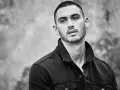 Hombre joven con un corte de pelo buzz cut, viste chaqueta vaquera oscura. Mirada intensa.