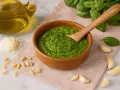 Frisches Pesto Genovese in einer Schale, umgeben von Pinienkernen, Parmesan, Knoblauch, Basilikum und Olivenöl.