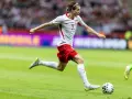 Jakub Kamiński w akcji, biegnie z piłką na boisku. Jego obecne drużyny to reprezentacja Polski i VfL Wolfsburg.