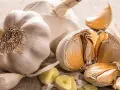 Mehrere Knoblauchzehen und ganze Knoblauchköpfe liegen auf einer hellen Oberfläche. Tipps zur Lagerung von Knoblauch.