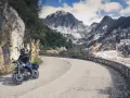 Un motociclista percorre una strada tortuosa tra le montagne della Toscana, con cave di marmo sullo sfondo.