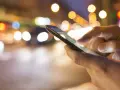 Hände bedienen ein Smartphone im nächtlichen Stadtverkehr. Tipps, um das iPhone schneller machen, sind hier vielleicht gesucht.