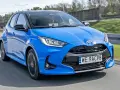 Błękitna, nowa Toyota Yaris z czarnym dachem pędzi po drodze.