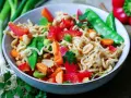 Bunter mie nudelsalat mit Erdnüssen, Zuckerschoten, Karotten und Paprika, garniert mit Petersilie.