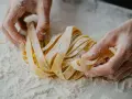 Mani infarinate lavorano un nido di tagliatelle fatte in casa, pronte per essere cucinate.