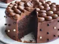 En saftig, klassisk chokladtårta med chokladfrosting och dekorationer av chokladkulor. En bit är bortskuren.