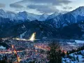 Zimowy wieczór w Zakopanem. Oświetlone miasto u stóp ośnieżonych Tatr, gdzieś w oddali widać stok narciarski. Marzą się bilety na Giewont.