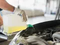 Mechanik w rękawiczkach nalewa płyn do spryskiwaczy do silnika samochodu. G12w.