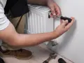 Man purga radiadores con un destornillador. Herramientas a su lado.