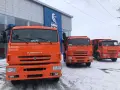 Trzy pomarańczowe, rosyjskie ciężarówki KAMAZ stoją przed budynkiem dealera.