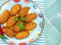 Croquetas doradas en un plato decorado con pimientos y perejil.