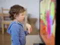 Chłopiec w niebieskiej bluzie z kapturem, jedząc kanapkę, ogląda telewizję. Czyżby to były najgorsze bajki dla dzieci?