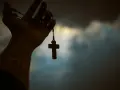 Dłoń trzyma paciorki różańca z krzyżem, symbolizując poszukiwanie prawdy w obliczu niepewności, jak agnostycyzm.