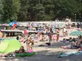 Tłoczna plaża nad jednym z **jezior blisko Wrocławia**. Ludzie opalają się, kąpią i odpoczywają na piasku.