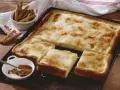 Ein köstlicher Rahmkuchen vom Blech, bestreut mit Zimt und Zucker. Daneben eine Schale mit Zimtstangen und Zimtpulver.