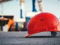 Czerwony kask budowlany na tle placu budowy. Symbol bezpieczeństwa pracy, który może wpływać na stopę procentową składek na ubezpieczenie wypadkowe.