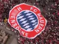 Ogromna flaga z herbem FC Bayern Monachium niesiona przez tłum kibiców.