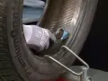 Mano guantata che esegue la riparazione gomma con un attrezzo, fissando una toppa interna.
