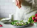 Une main saupoudre des graines sur une salade fraîche. Une idée pour une recette de radis noir.
