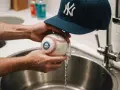 Czyszczenie czapki z daszkiem i piłki baseballowej pod bieżącą wodą.