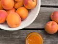 Ein Korb voller reifer Marillen, daneben ein Glas Marillenmarmelade. Was sind Marillen? Süße Früchte, perfekt für Marmelade!