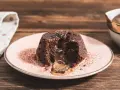 Coulant de chocolate con centro líquido y cremoso, espolvoreado con cacao en polvo sobre un plato rosa.