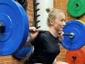 Kvinna utför squats med hantlar. Hon har en skivstång på axlarna med blå viktskivor.