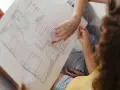 Dwie osoby analizują plan mieszkania. Jedna z nich wskazuje palcem na rysunek, dyskutując, czy parter to kondygnacja.
