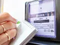 Dłoń z pierścionkami zapisuje odczyt licznika energii elektrycznej, by sprawdzić rachunek za prąd.