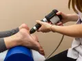 Fizjoterapeuta stosuje terapię falą uderzeniową na stopę pacjentki, by złagodzić ból.
