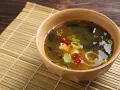 Aksamitna zupa miso z tofu, wodorostami, szczypiorkiem i papryczką chili, podana w ceramicznej miseczce na bambusowej macie.