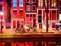 Nocna czerwona ulica Amsterdamu, z oświetlonymi oknami i kanałem odbijającym światła.