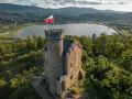Kamienny zamek księcia Henryka z polską flagą na wieży, otoczony lasem, z widokiem na jezioro i góry. Punkt widokowy zaprasza do podziwiania krajobrazu.