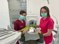 Dwie dentystki w maseczkach i rękawiczkach z uśmiechniętym pacjentem w gabinecie stomatologicznym.