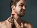 Hombre con piel irritada afeitado, se rasca el cuello con una navaja de afeitar azul.