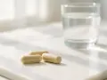 Tre capsule beige e un bicchiere d'acqua su una superficie chiara. Scopri quali sono i probiotici per il tuo benessere.