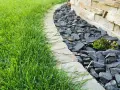 Ein Gartenweg mit frisch gemähten Rasen und grauen Bruchsteinen, die den Rand eines Beetes mit einer Sukkulente markieren. Die Pflastersteine schneiden eine klare Linie.