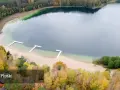 Jesioro Płotki jesienią. Piękna plaża, drewniane pomosty i kolorowe drzewa otaczają spokojną taflę wody.