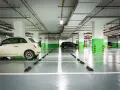 Jasny samochód i ciemny SUV stoją na parkingu podziemnym. Widać wyraźnie wyznaczoną szerokość miejsca parkingowego.