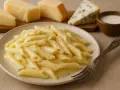 Penne w sosie serowym, obok kawałki sera, w tym gatunek owczego sera, i mleko.
