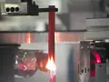 A red acrylic rod is tested for how acrylic fire resistant it is, with a flame licking its base.