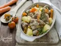 Un invitante spezzatino in bianco con patate e carote, guarnito con rosmarino e alloro. Accanto, pomodorini e carote fresche.