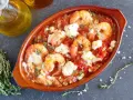 Gamberoni al guazzetto in terracotta, con pomodoro, formaggio fuso e timo. Un piatto invitante pronto per essere gustato.