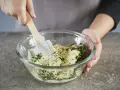 Hände mischen Kräuter und Butter in einer Schüssel. Perfekt, um Kräuterbutter selber zu machen.