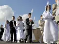 Kinder in festlicher Kleidung, was zieht man zur Kommunion an? Mädchen in weißen Kleidern, Jungen in Anzügen, alle tragen Kerzen.