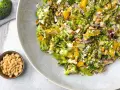 Ein bunter gekochter Brokkoli-Salat mit Pinienkernen, Feta und Orangenstücken auf einem Teller.