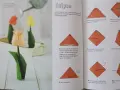 Vackra vika pappersblommor i form av tulpaner, en klassiker inom origamikonsten. En orange tulpan i förgrunden, med en röd och en gul i bakgrunden.