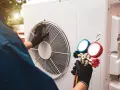 Technicien effectuant l'entretien d'une pompe à chaleur air/air, vérifiant la pression avec un manomètre.